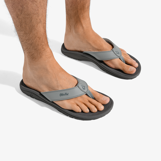 Man wearing gray and black thong sandals with contoured footbeds and logo detail on strap.