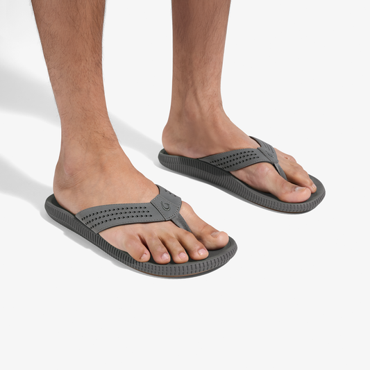 Pair of gray flip-flop sandals with textured soles and perforated straps worn on bare feet.