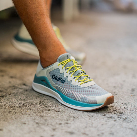 Running shoe with white sand and seagreen color blocking, yellow laces, worn on foot outdoors.