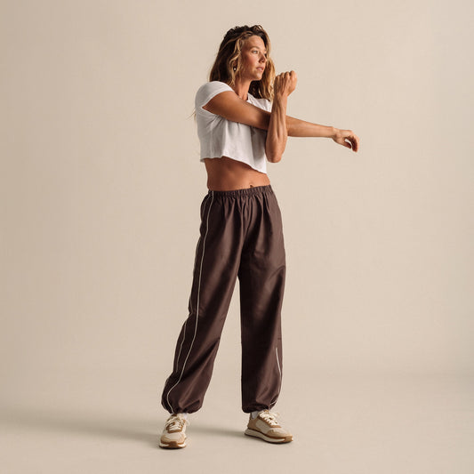 Woman wearing white cropped t-shirt and brown elastic-waist pants with cream sneakers.
