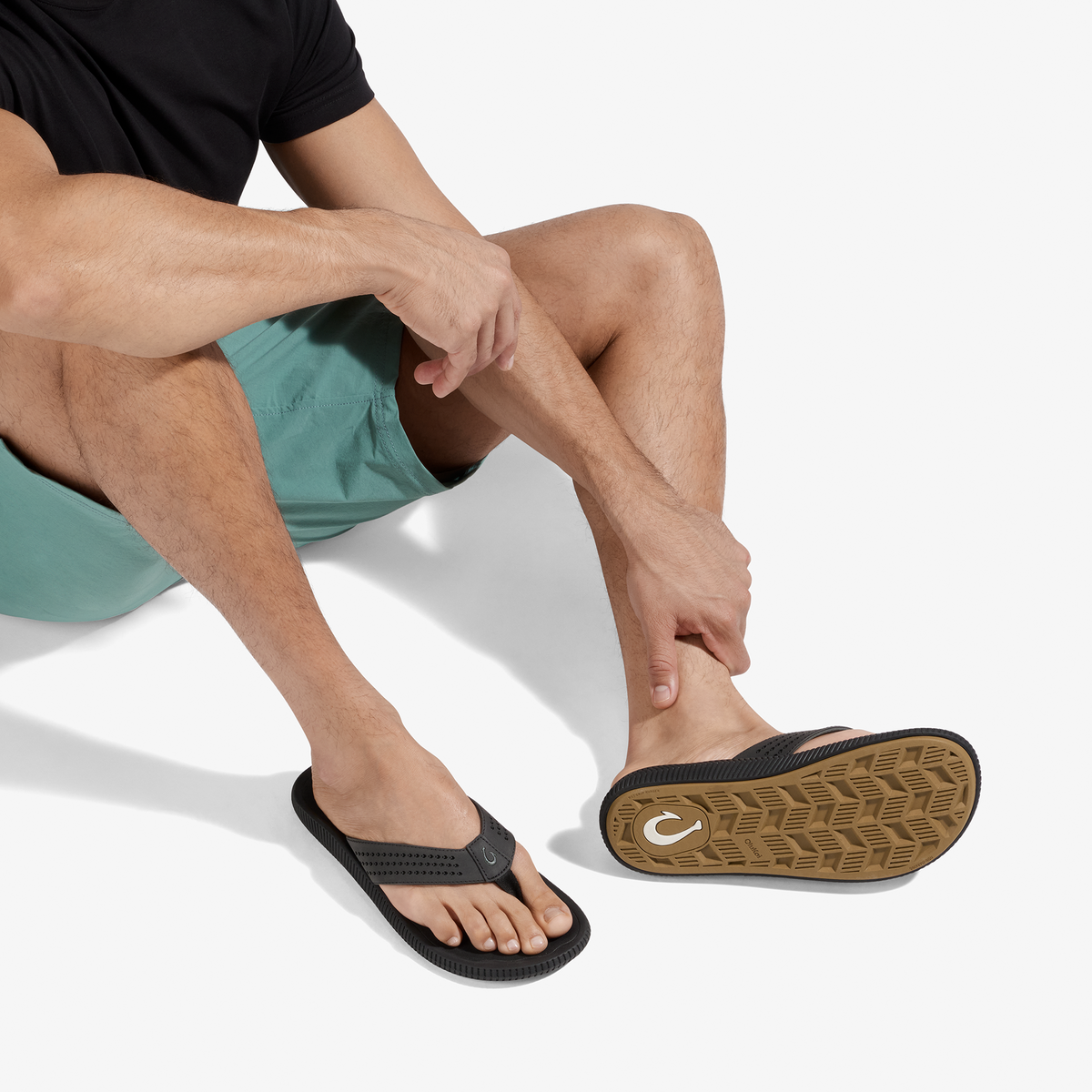 Man wearing teal shorts and black thong sandal with textured sole, shown from waist down.