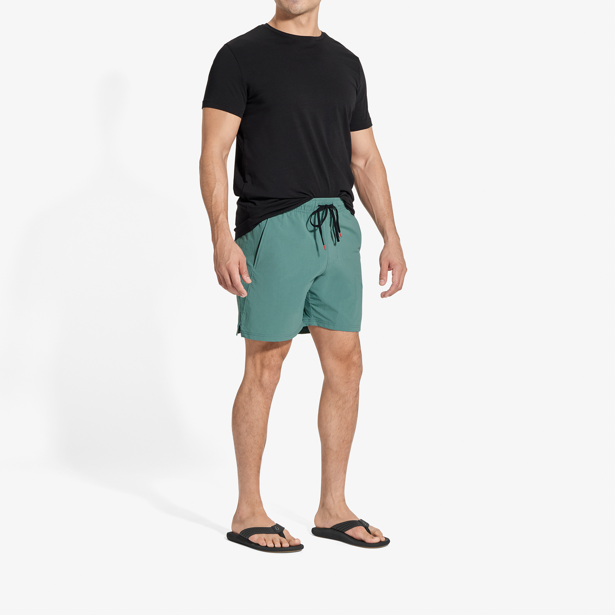 Man wearing black short-sleeve t-shirt, teal drawstring shorts, and black slide sandals.