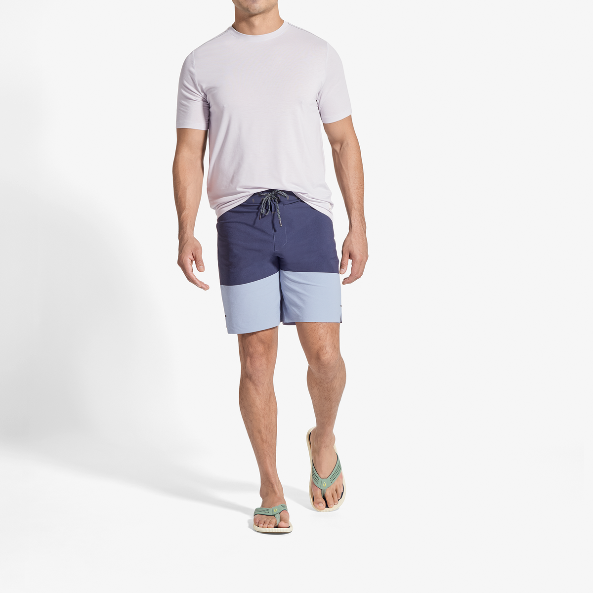 Man wearing light pink t-shirt and color-block shorts in navy and light blue with green sandals.