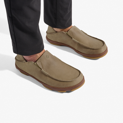 Pair of tan slip-on loafers with brown soles worn with black pants.