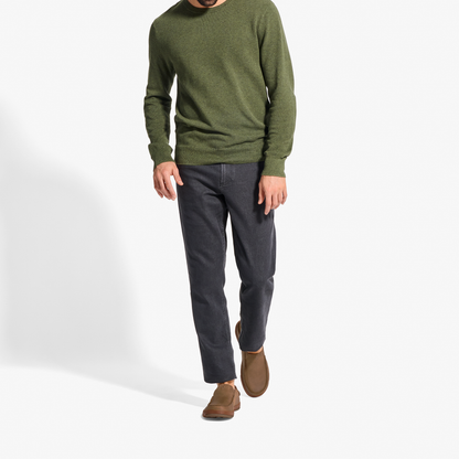 Man wearing olive green crew neck sweater, dark jeans, and tan suede slip-on shoes.