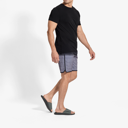 Man wearing black t-shirt, blue shorts, and gray and black slide sandals.