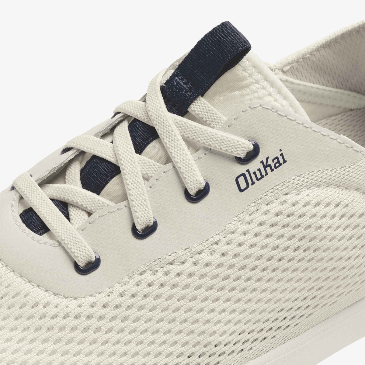 White canvas sneaker with dark blue laces and heel tab, Olukai branding on side.