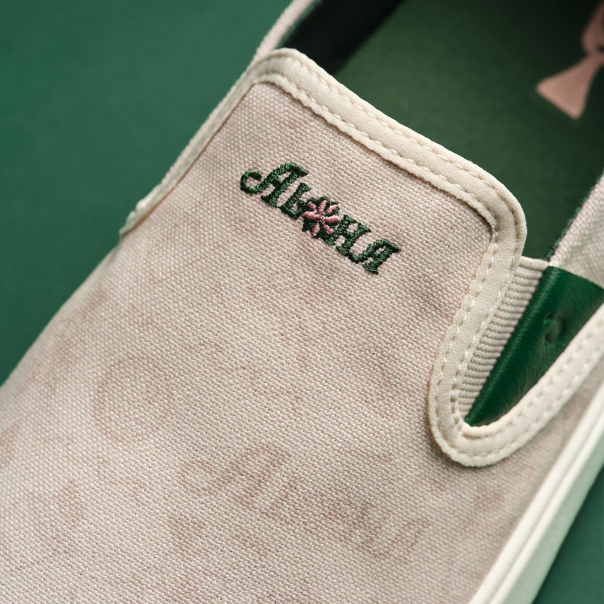 Cream canvas slip-on shoe with green stripe and embroidered brand text on the side.