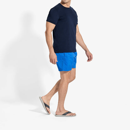 Man wearing dark navy short-sleeve t-shirt and blue swim shorts with slide sandals.