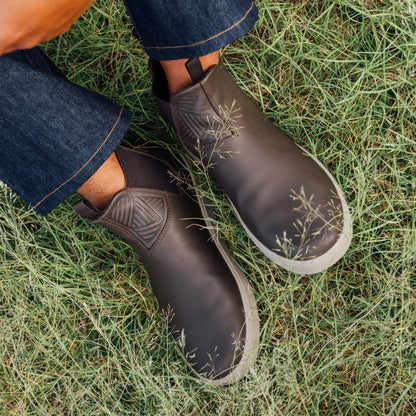 Dark Java slip-on boots with botanical leaf pattern worn on grass with jeans and black socks.