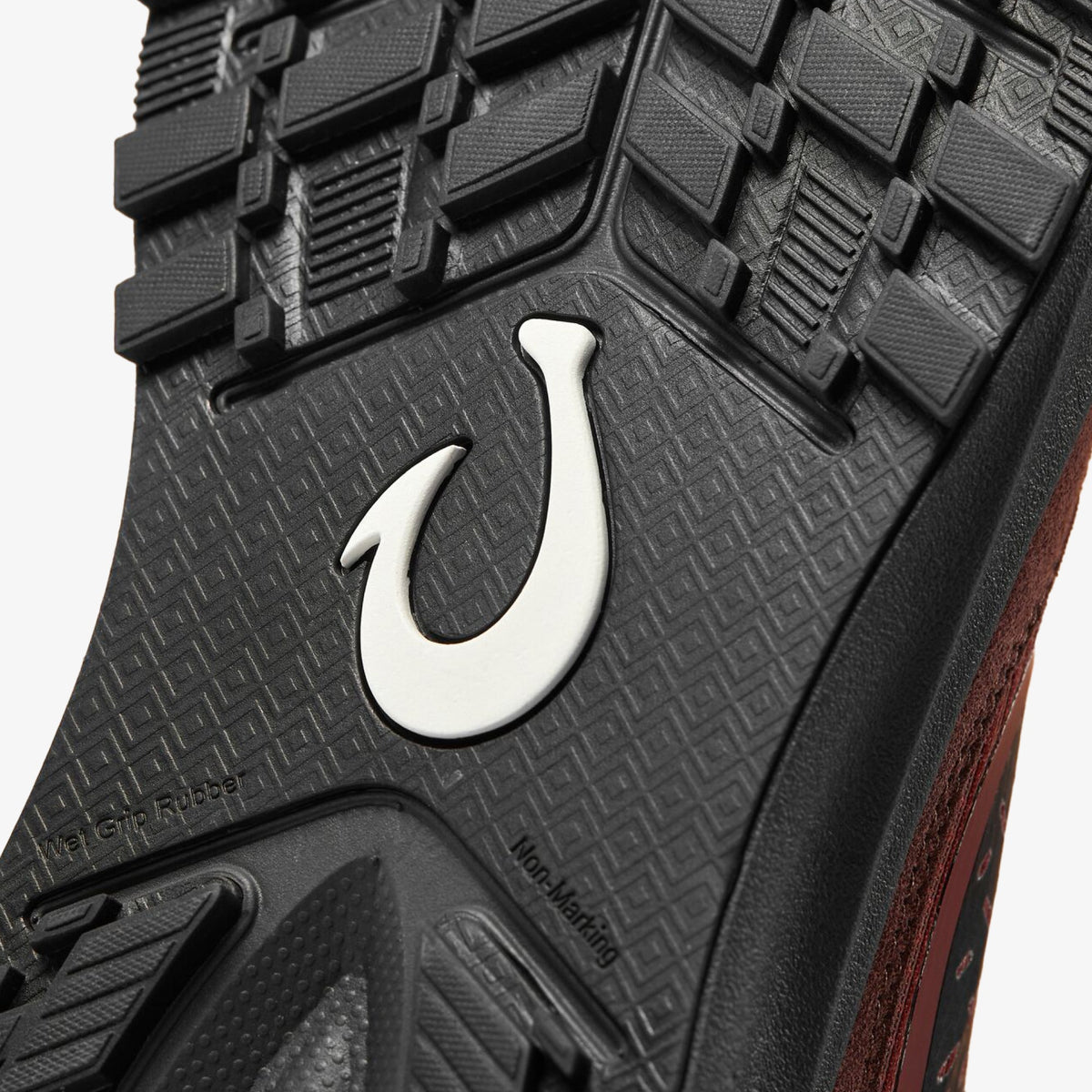 Black rubber sole with white hook logo and red clay-colored side panel visible.