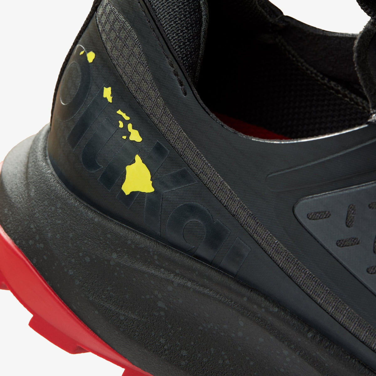 Black athletic shoe with yellow Hawaiian Islands design on heel and red sole detail.