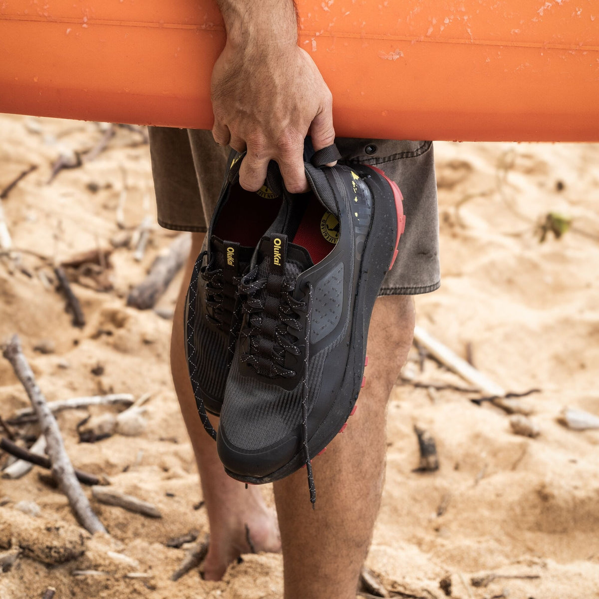 Black lace-up hiking shoe with textured mesh upper held in hand over rocky terrain.