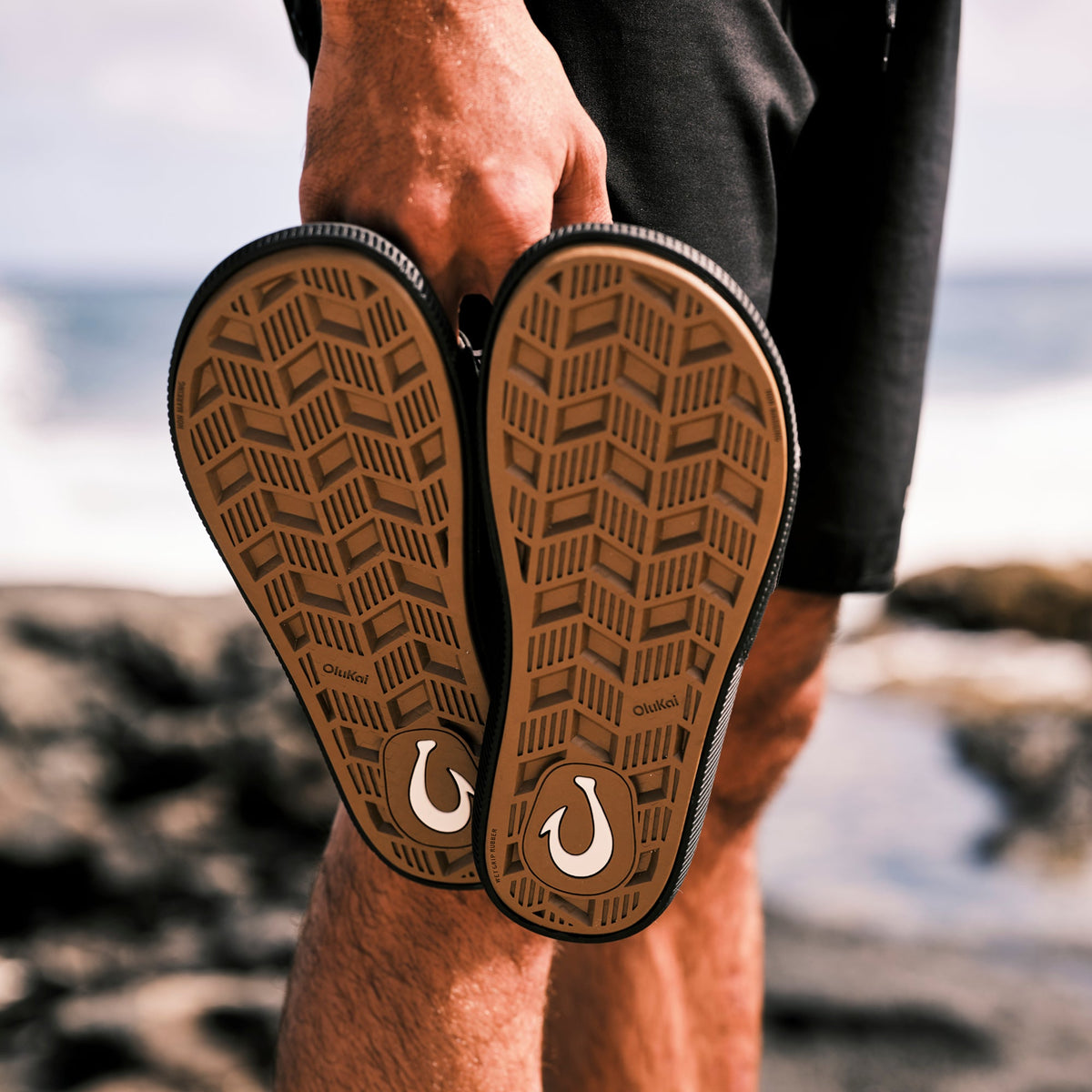 Lava Rock slide sandals with tan soles featuring geometric pattern and white logo, worn by person at beach.