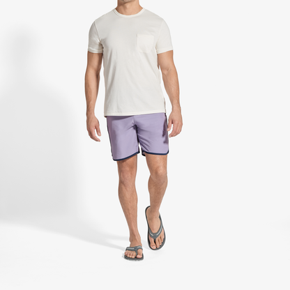 Man wearing cream short-sleeve t-shirt with chest pocket and lavender shorts with dark trim.
