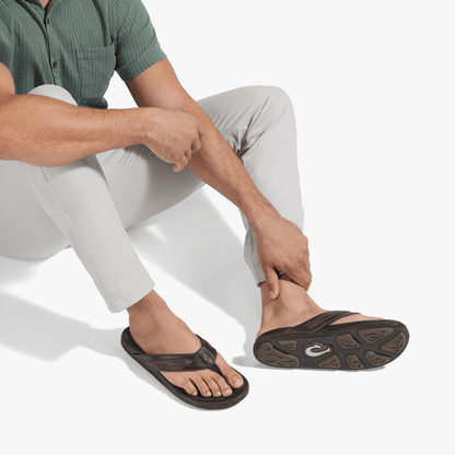 Man wearing dark Java thong sandal with tan sole, paired with light gray pants and green button-up shirt.