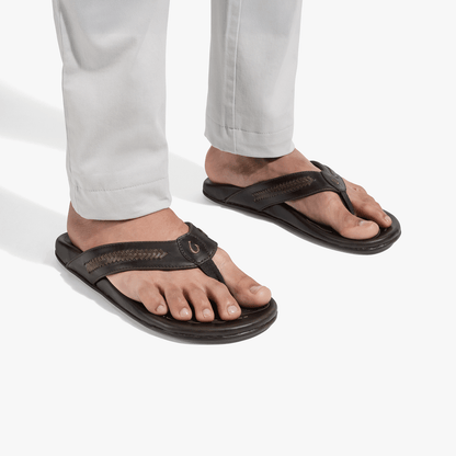 Black flip-flops with woven straps worn with white pants.