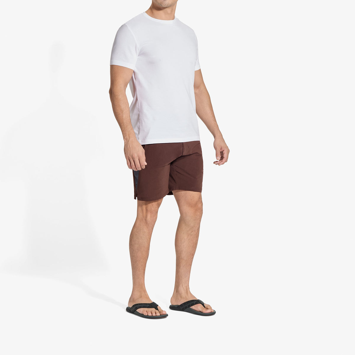 Man wearing white short-sleeve t-shirt, dark brown shorts, and black slide sandals.