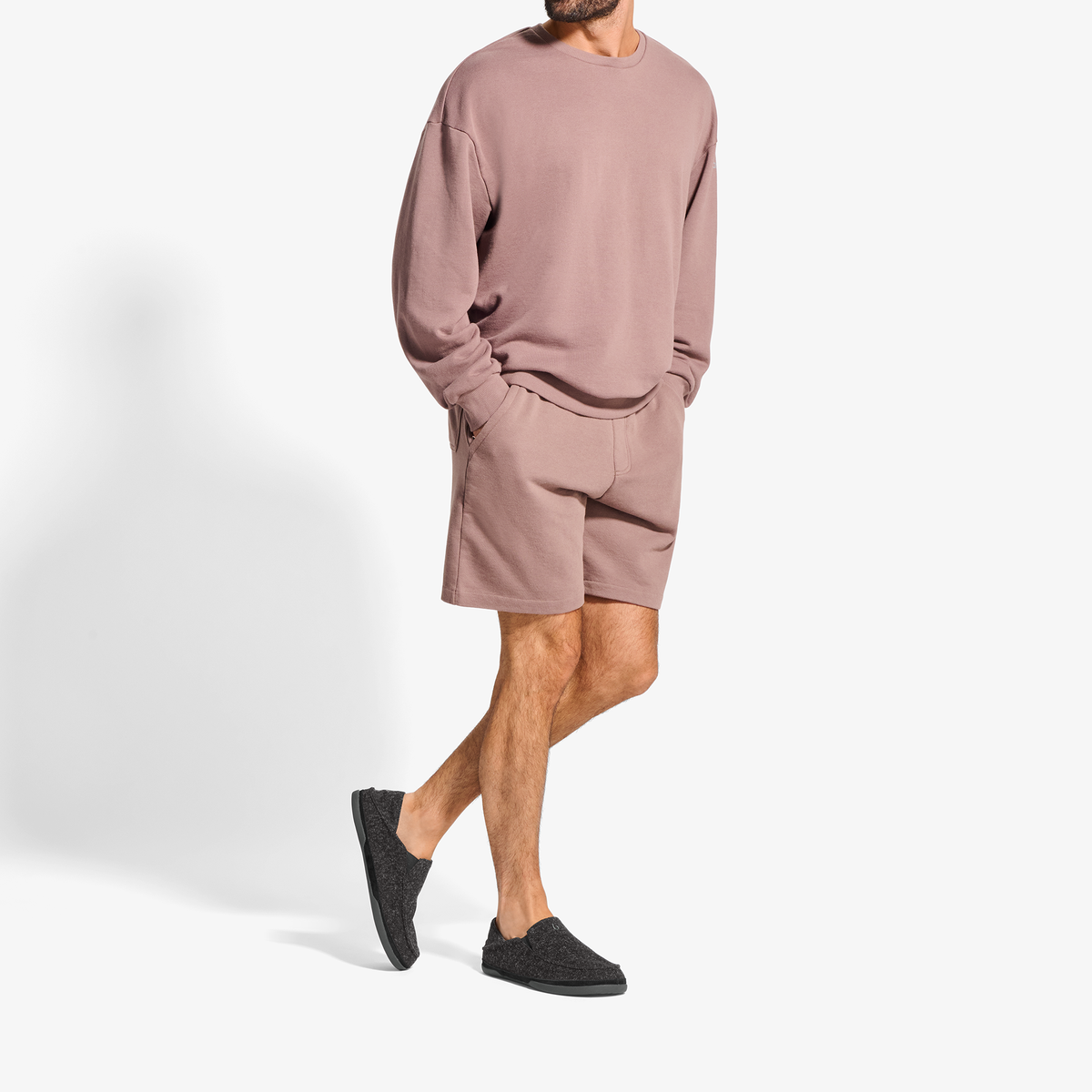 Man wearing mauve crew-neck sweatshirt and matching shorts with black slip-on shoes.