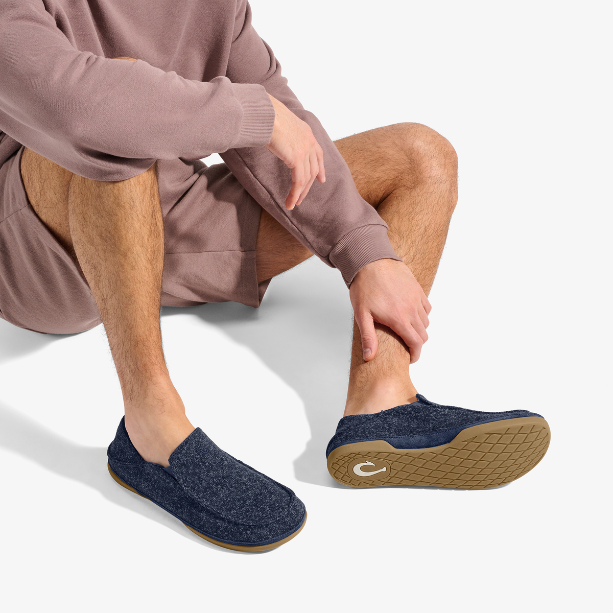 Person wearing dark blue wool slippers with tan sole, styled with mauve shorts and hoodie.