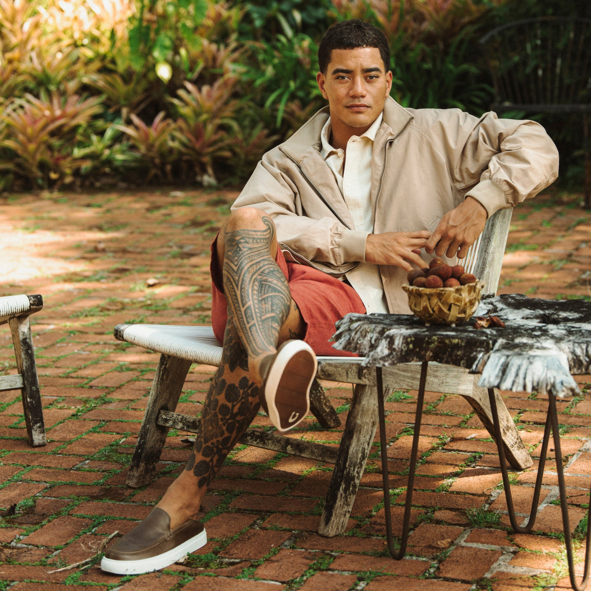 Walnut slip-on shoe with white sole, worn by man seated outdoors.