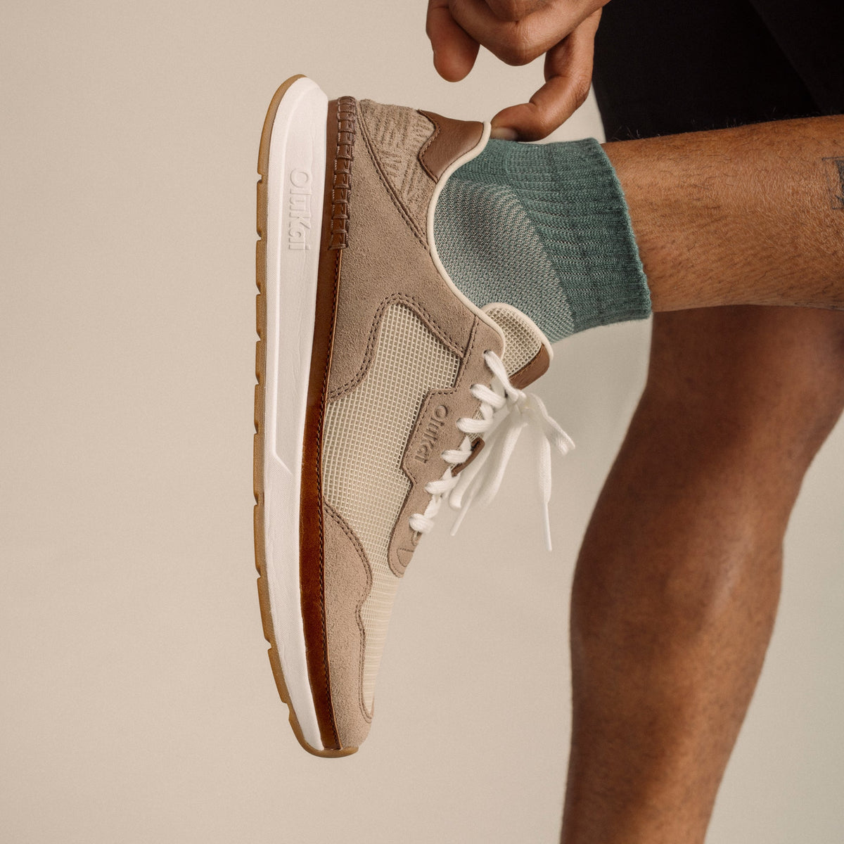 Ecru and taupe grey lace-up sneaker with white sole, worn with green socks.