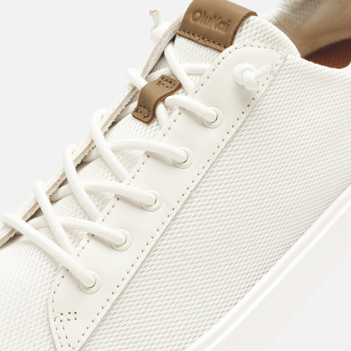 White canvas sneaker with tan leather heel tab and white laces, shown from side angle.