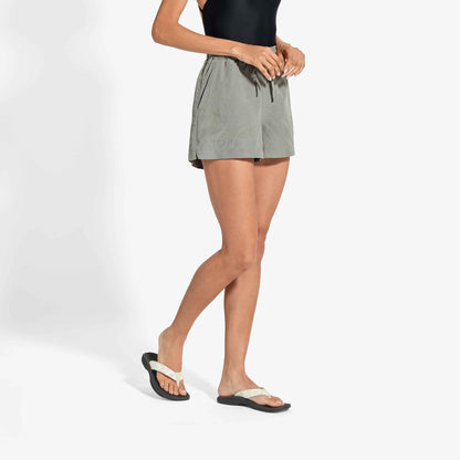 Woman wearing sage green shorts with drawstring waist and black flip-flops.