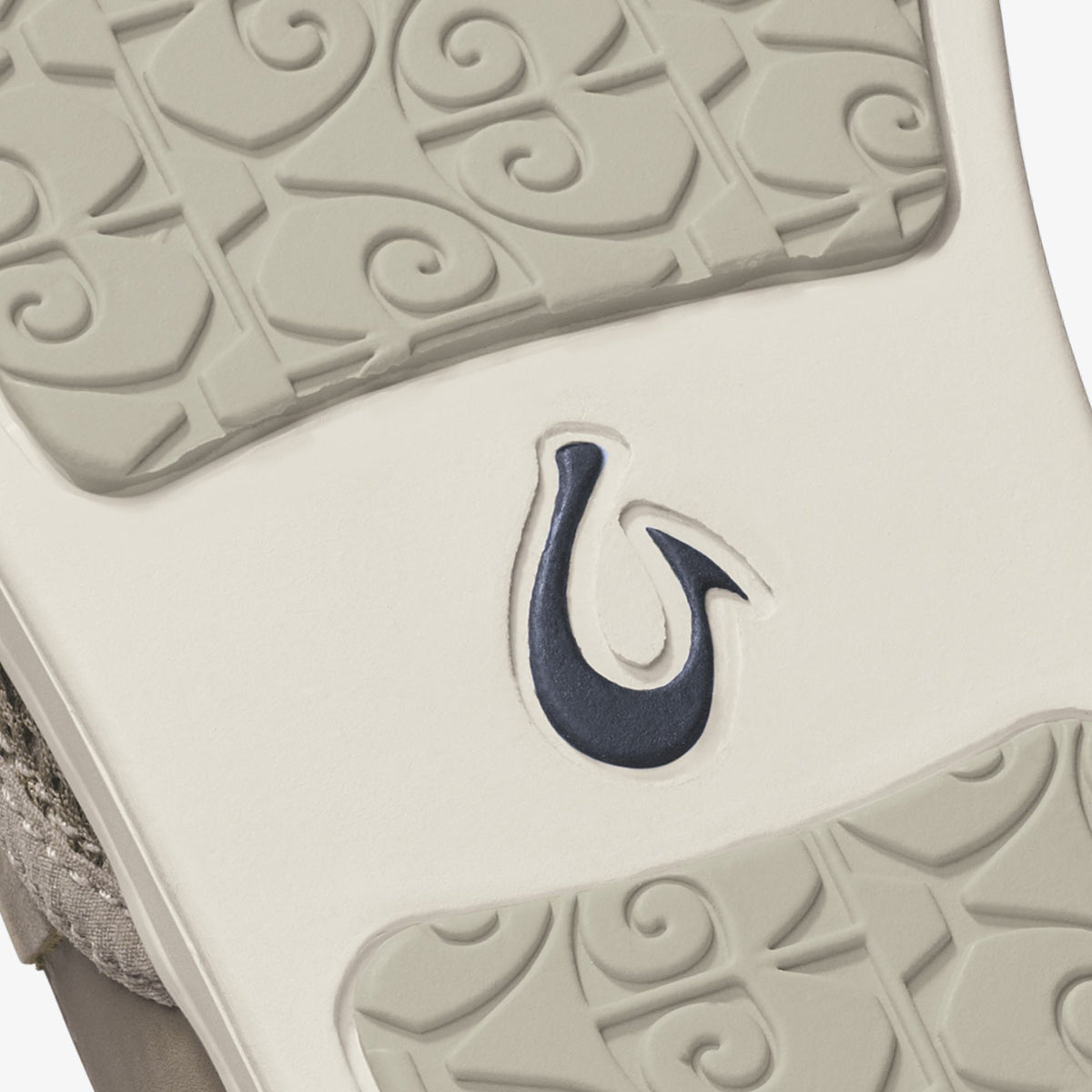 Taupe grey shoe sole with navy hook logo and embossed scroll pattern detail.