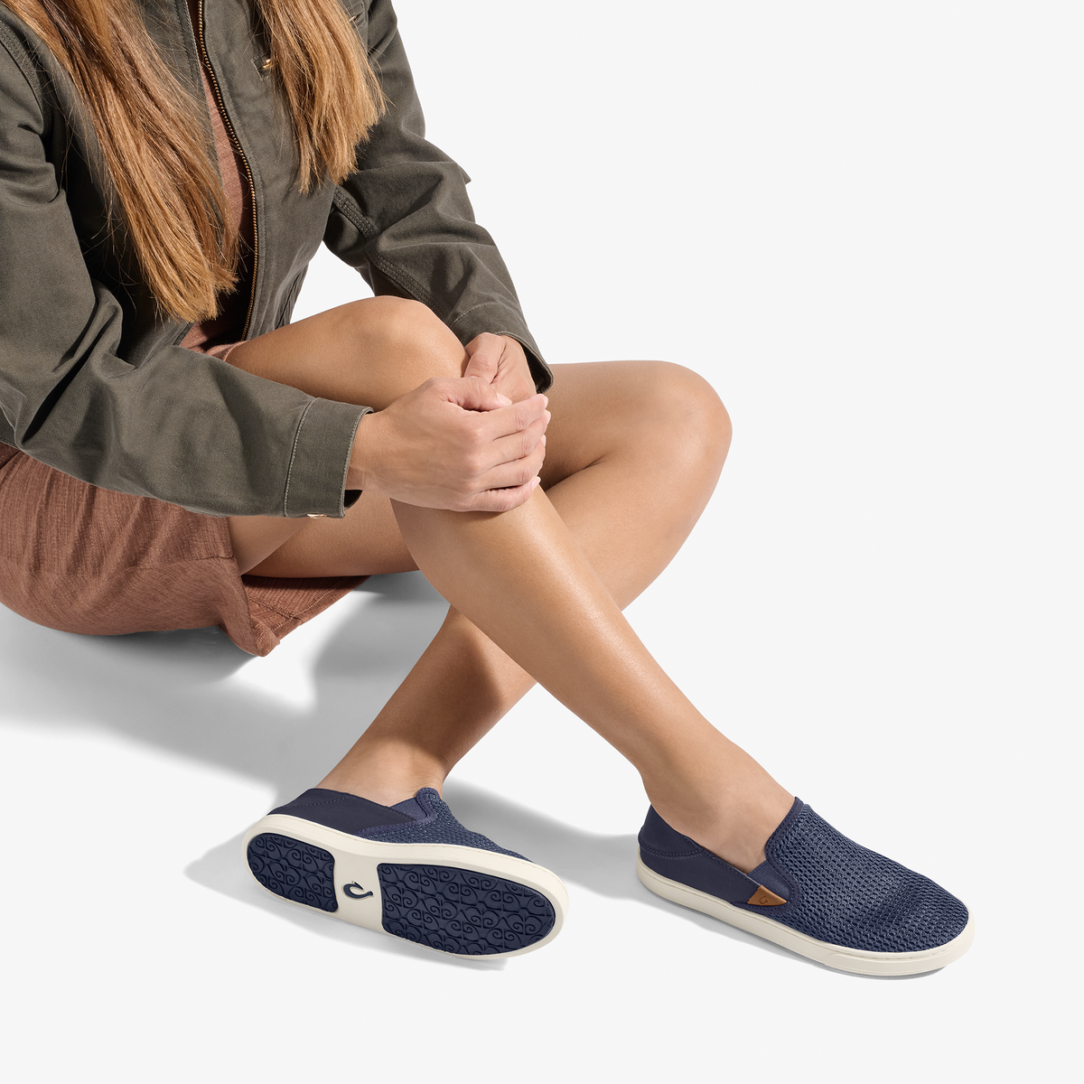 Woman wearing dark blue slip-on shoe with cream sole and textured upper, paired with casual shorts and jacket.