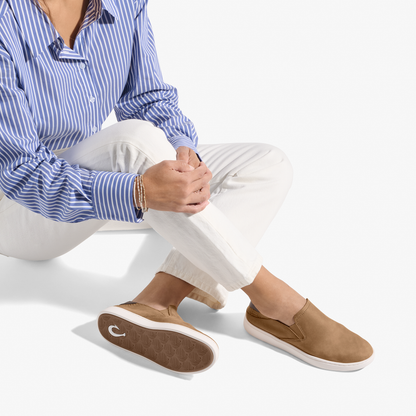 Tan leather slip-on shoe with white sole, worn with white pants and blue striped shirt.