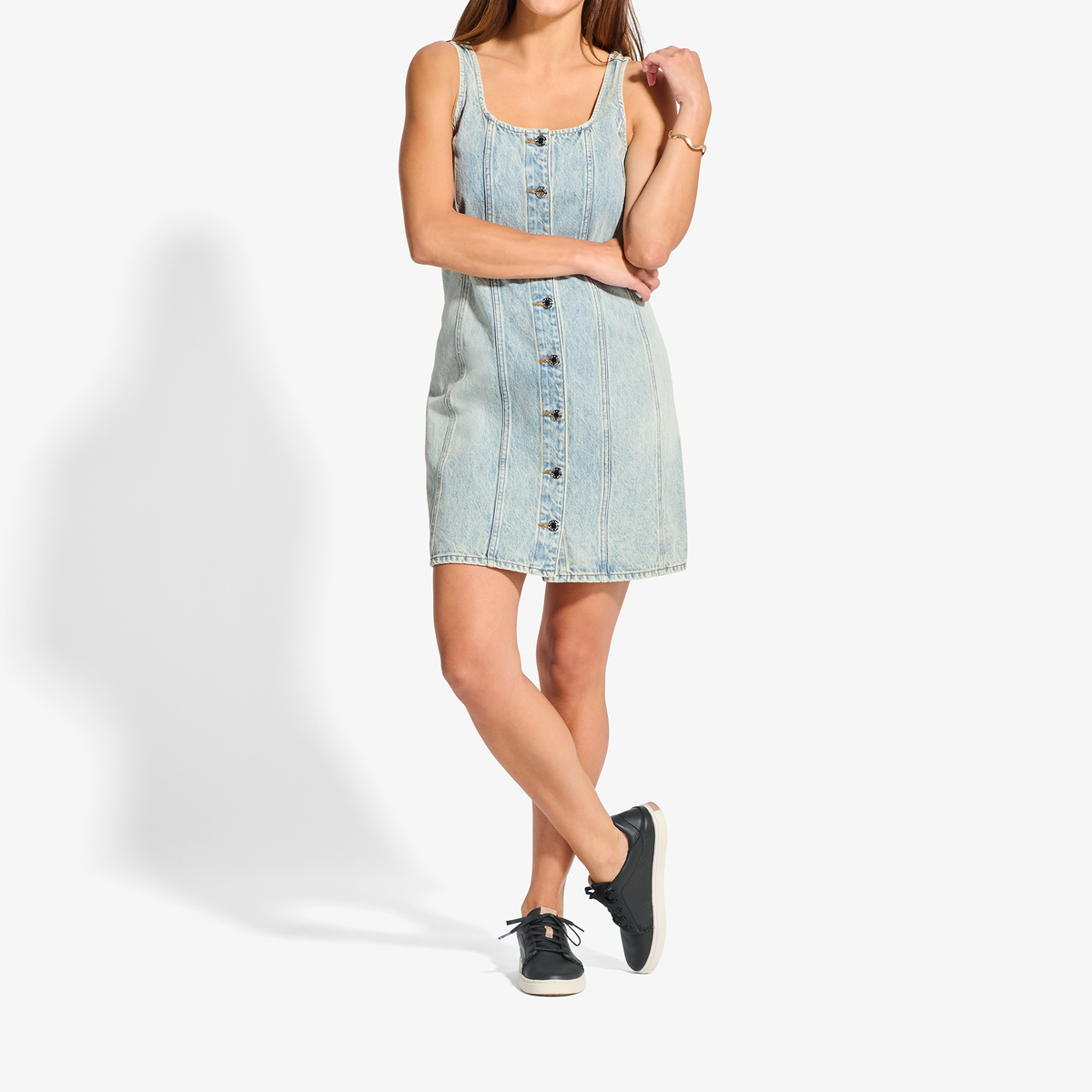 Light wash denim sleeveless dress with button front, styled with black canvas sneakers.