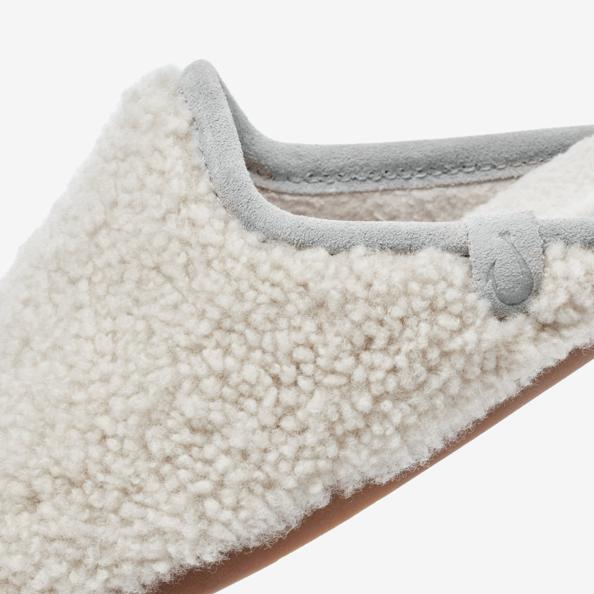 Mule slipper with cream textured fleece upper and ash gray suede trim, showing interior lining and brown sole.