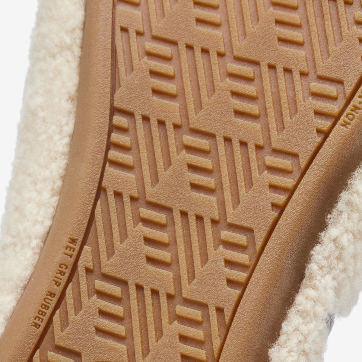 Tan leather sole with geometric tread pattern and cream-colored textile upper visible.