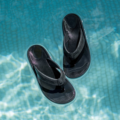 Black flip-flop sandals with textured footbeds and curved straps, shown floating on water surface.