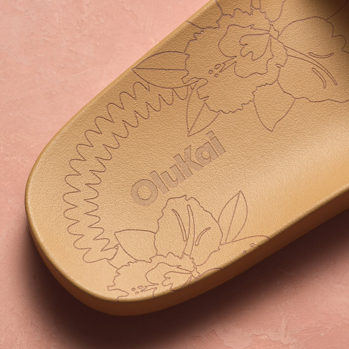 Warm sand-colored oval object with embossed floral and leaf designs and "Ohikar" text on soft pink background.