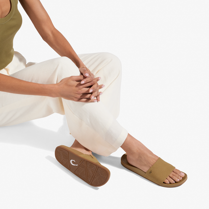 Person wearing tan slide sandals with crosshatch pattern and brown soles, seated in cream pants.