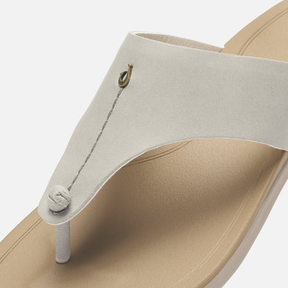 Cream-colored thong sandal with tan sole, metal loop detail, and adjustable cord closure.