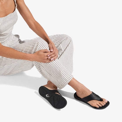 Black slide sandal with curved footbed and thong strap worn with striped pants.