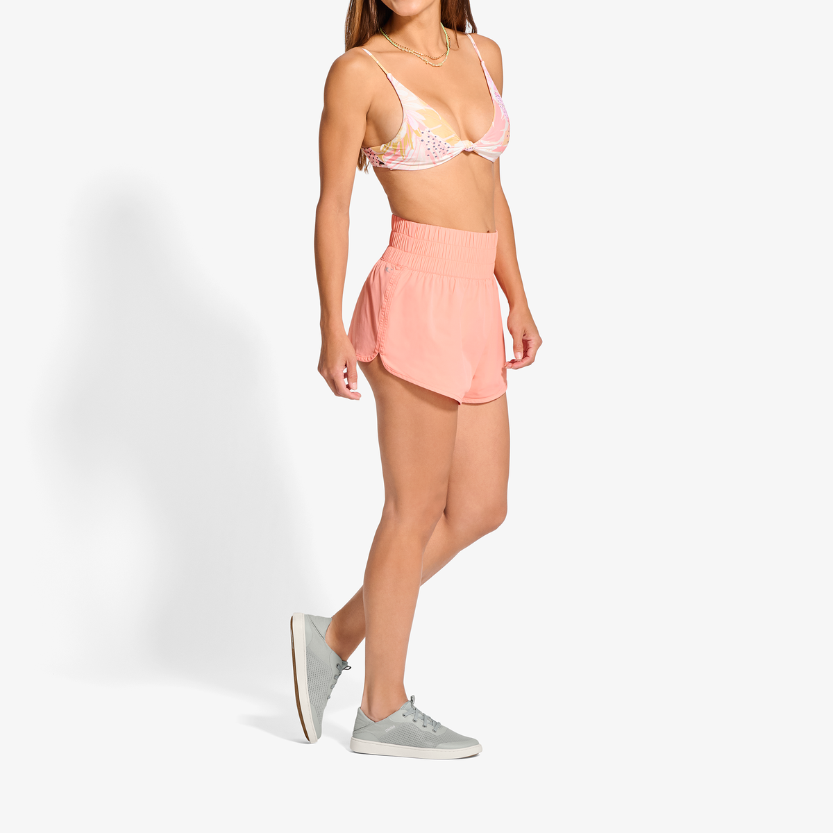 Woman wearing pink bikini top with white polka dots and matching pink ribbed skirt with grey sneakers.
