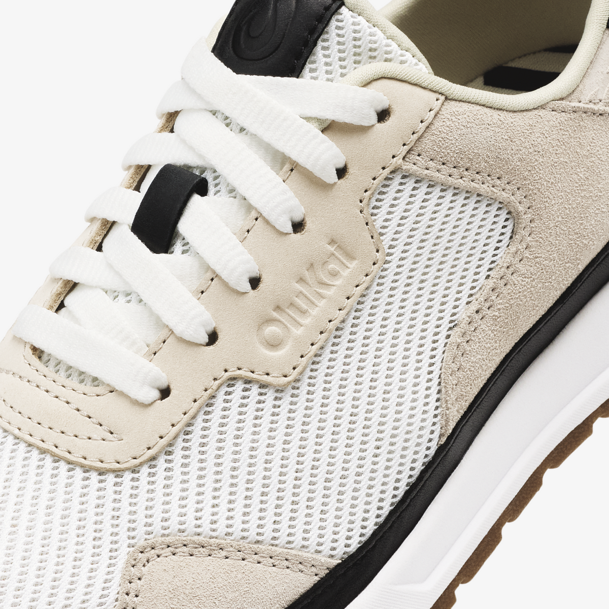 Closeup of cream and white lace-up sneaker with mesh and suede panels, white laces, and black heel tab.