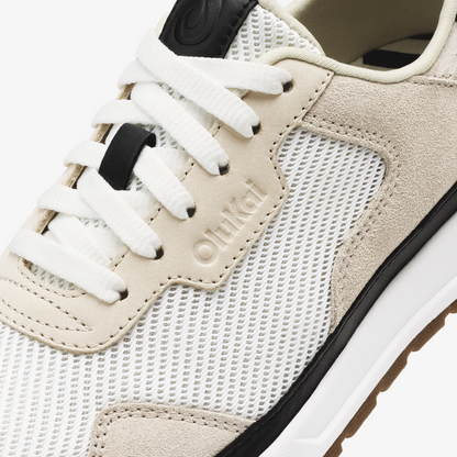 Closeup of cream and white lace-up sneaker with mesh and suede panels, white laces, and black heel tab.