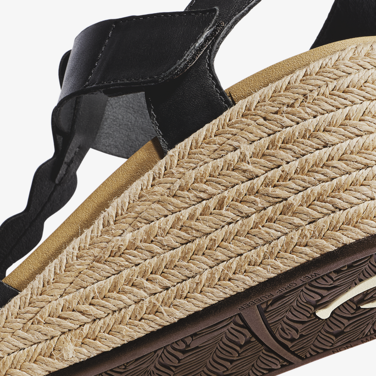 Black leather sandal with woven tan jute straps and dark sole, showing ankle detail and textured footbed.
