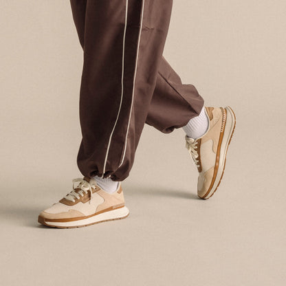 Two cream and tan sneakers with white socks worn with brown track pants.