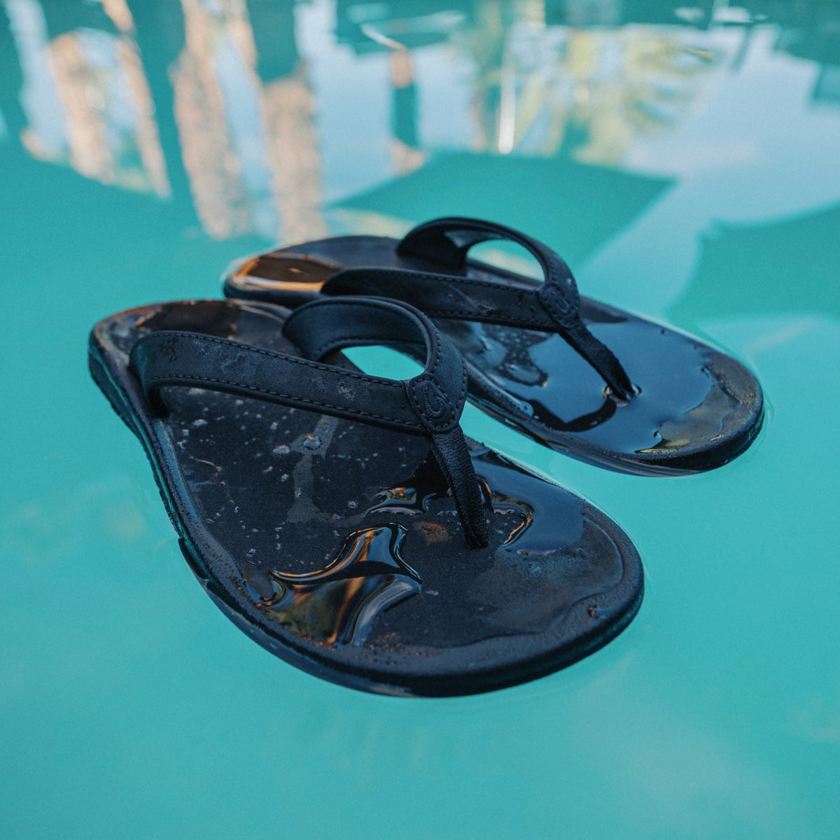 Pair of black thong sandals with textured soles, displayed on a turquoise surface with water droplets.