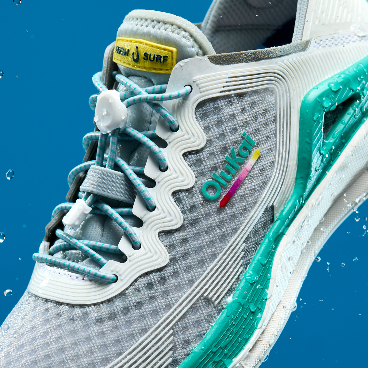 Grey and white water shoe with turquoise accents, white ribbed sole, patterned laces, and yellow "Ahi Surf" heel tag.