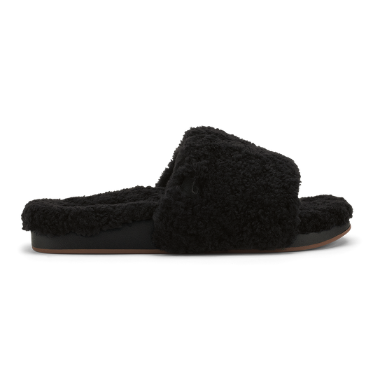 Black fuzzy slip-on slipper with cushioned sole and fluffy upper, shown in profile view.