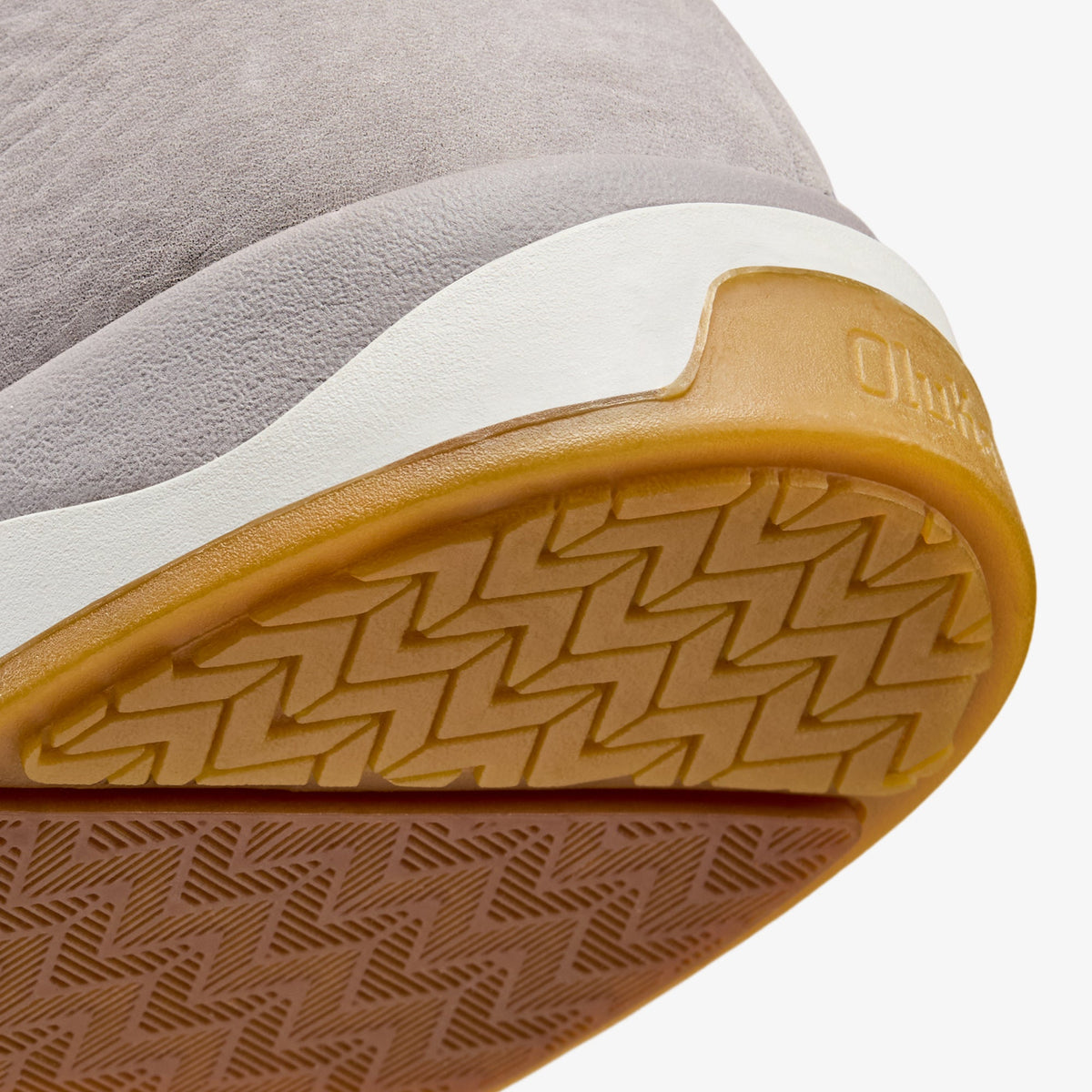 Closeup of shoe sole showing gray textile upper, white midsole, and tan rubber outsole with geometric tread pattern.